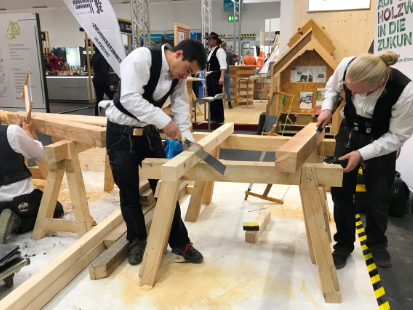 Mehrere Gesellen bearbeiten ein Holzgerüst auf der Baumesser HAUS, 2020.