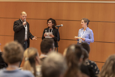 Ein Mann und zwei Frauen stehen auf der Bühen und sprechen