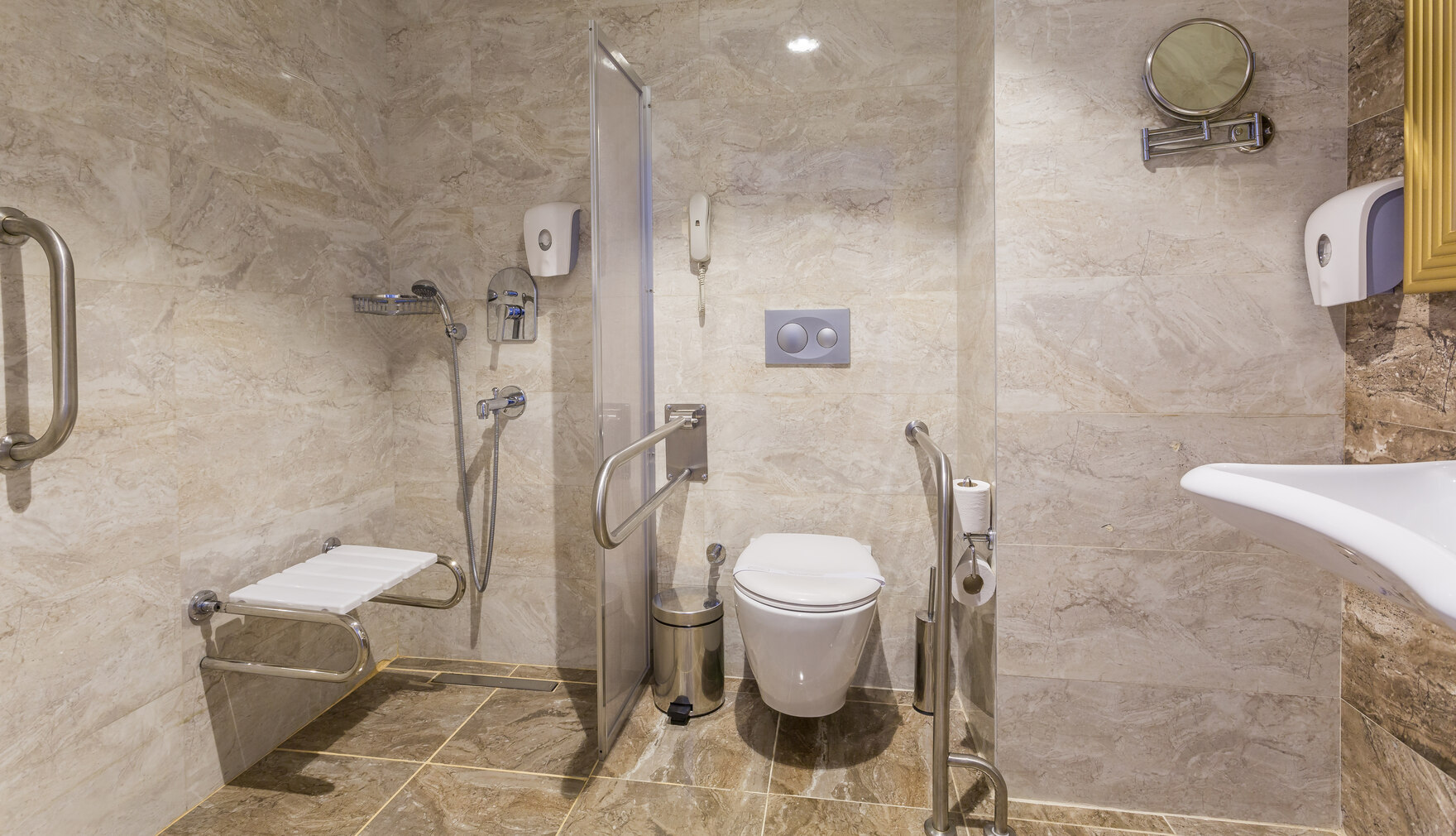 modernes, barrierefreies Badezimmer mit offener, ebenerdiger Dusche mit Haltergriff und Sitz sowie Handläufen rechts und links vom WC